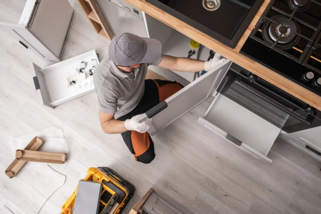 Overhead view of a person fitting a white base-cabinet door beside a kitchen sink