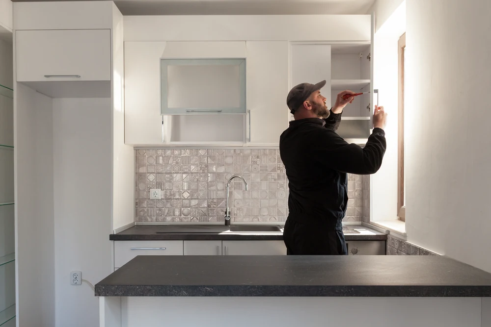 Person adjusting a white upper cabinet in a kitchen with patterned tile backsplash