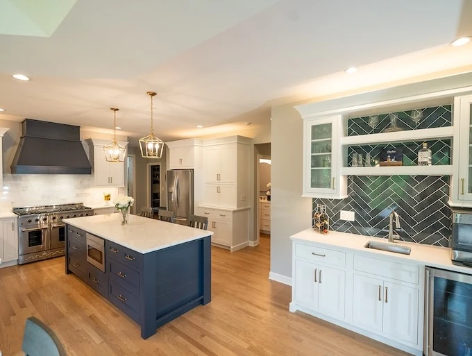 White kitchen with a navy island and a dark green herringbone tile backsplash