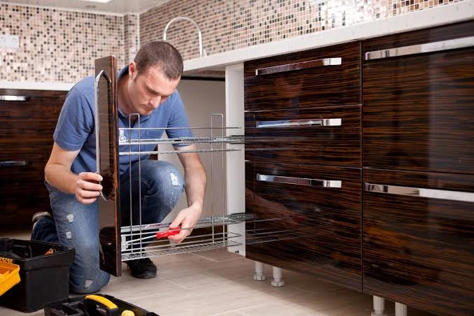 Person fitting a pullout wire storage basket into dark wood kitchen cabinetry
